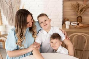 sons with mom are sitting at the table in a cozy kitchen decorated with wood. happy family going to eat at home at the table photo
