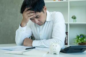 Stressed and headache asian man with large bills or invoices no money to pay to expenses and credit card debt. shortage, Financial problems, mortgage, loan, bankruptcy, bankrupt, poor, empty wallet photo