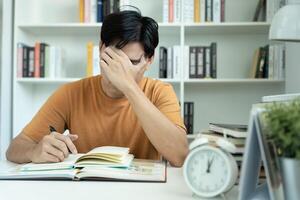 Asian student man have anxiety because of exams, male prepare for test and learning lessons in the library. stress, despair, haste, misunderstanding reading, discouraged, expectation, knowledge, tired photo