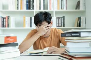 Asian student man have anxiety because of exams, male prepare for test and learning lessons in the library. stress, despair, haste, misunderstanding reading, discouraged, expectation, knowledge, tired photo