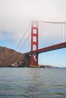 Discover the mesmerizing Golden Gate Bridge in San Francisco, California. Captured from water level, this iconic landmark stands tall with vibrant red orange against a calm blue sky. photo