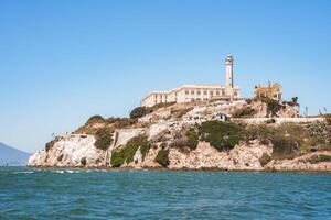 Alcatraz Island view from water in San Francisco Bay, California, USA. Rugged coastline, former prison, iconic lighthouse, clear sky, calm water, sparse vegetation, historical landmark. photo