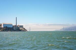 View of Alcatraz Island in San Francisco Bay, CA, USA. The Federal prison buildings and the Golden Gate Bridge are visible in the backdrop, creating a contrast between nature and history. photo