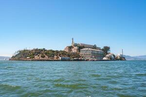 Sunny view of Alcatraz Island in San Francisco Bay, California, USA. Features former prison complex with main cellhouse, lighthouse, and serene waters. photo