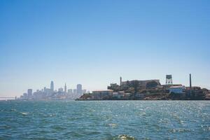 Clear day view of Alcatraz Island from the water, showcasing the infamous prison with cityscape of San Francisco in the background. Serene atmosphere. photo