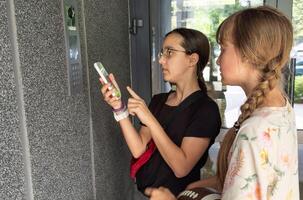 two teenagers getting access to the building by attaching smartphone to intercom. Concept of modern security technologies for access and smart home photo