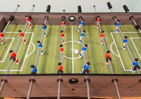 Classic Foosball Table Game With Players in Red and Blue Jerseys During Daytime Indoor Match. Close-up view of foosball table featuring red and blue jersey players positioned for daytime indoor game. photo