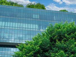 Eco-friendly building in modern city. Sustainable glass office building with trees for reducing carbon dioxide. Office building with green environment. Corporate building reduce CO2. Net zero emission photo
