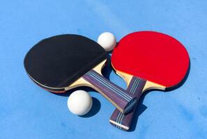 Two table tennis rackets and balls on a blue table with net. photo