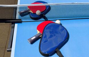 Two table tennis rackets and balls on a blue table with net. photo