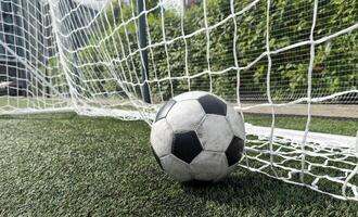 Soccer football in Goal net with green grass field. photo