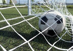 Soccer football in Goal net with green grass field. For sport concept. photo
