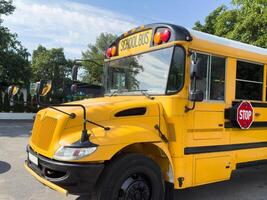 Shot of retro-styled yellow school bus with extended red stop sign standing still on serene road, empty vehicle with no driver awaiting children to boarding, transportation concept, copy space photo