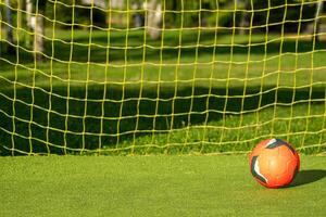 red soccer ball with the yellow net of a goal on an artificial grass football field photo