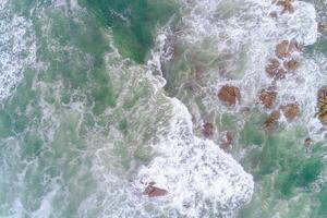 foam from waves breaking on a rocky coast, aerial overhead view with drone photo