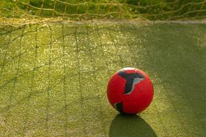 red soccer ball with the yellow net of a goal on an artificial grass soccer field photo