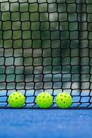 three green pickleball balls next to the net of a pickleball court, new racket sport photo