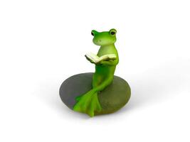 Decorated miniature frog sitting on a rock and reading a book on a white background photo