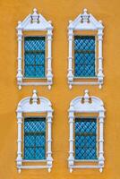 Close up view on a facade of ancient orange building with four windows with lattice and carved white stone platbands as texture photo