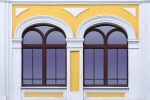 Close up view on a facade of white yellow ancient building with two arched windows as texture photo