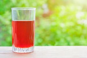 Summer concept. View on a glass with red juice on a wooden table, illuminated by sunlight on a background of green garden in bokeh with copy space photo