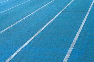Fragment of blue synthetic surface of running tracks of athletics stadium with white lines as texture, background photo
