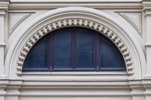 Close up view on a semicircular window on a facade of white stone ancient building with carved decor photo