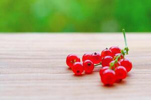 A branch of red currant on a wooden table on a background of green garden in bokeh with copy space photo