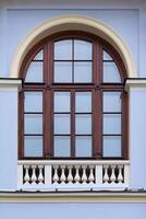 Close up view on a arched window with wooden frame and decorative white fence on bottom on a facade of blue ancient building photo