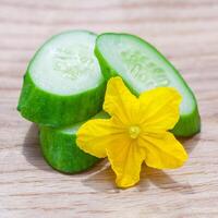 Close up view on a slices of fresh cucumber with yellow flower lying on a wooden table photo