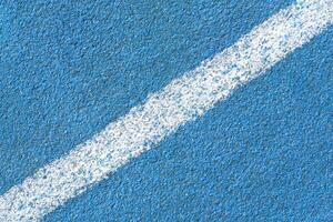 Blue synthetic tartan surface of a track of athletics stadium with white diagonal line as texture, background photo