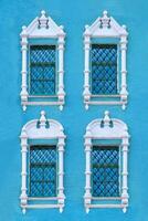 Close up view on a facade of ancient blue building with four windows with carved white stone platbands as texture photo