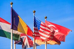 Close up view of a flags of different countries flutters in the wind against a blue sky photo