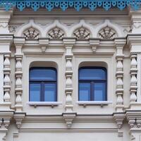 Close up view on a facade of white ancient building with decorative ornaments and two windows photo