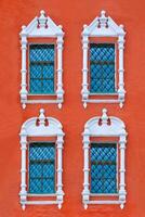 Close up view on a facade of ancient red building with four windows with carved white stone platbands as texture photo