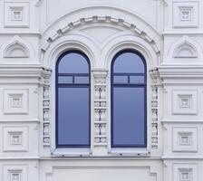 Close up view on a facade of white ancient building with decorative ornaments and two-part arched windows as texture photo