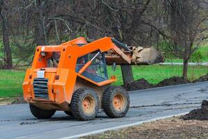 Orange Skid steer loader is on the road. Works on the improvement of the park area. photo