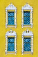 Front view on a facade of ancient yellow building with four windows with carved white stone platbands as texture photo