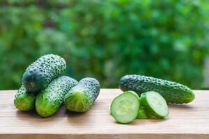 View on a pile of fresh cucumbers, whole and sliced on a wooden board on a background of green garden in blur with copy space photo