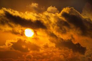 Dramatic view of a dark silhouettes of clouds in the orange sky illuminated by the rising sun photo