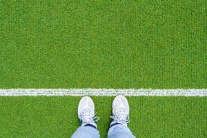 Top view of legs in sports shoes in front of the white line on the green sports ground with copy space photo