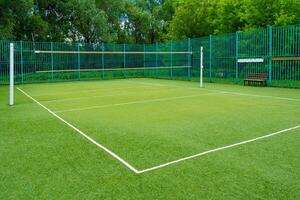 The sports playground in the park with artificial grass and a stretched net on a background of green trees photo