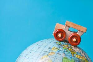 Wooden toy car on a globe on azure background with copy space. The concept of tourism, travel photo