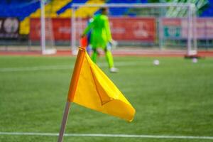 Close up view of a yellow corner flag on the football field on a background of the players in blur photo