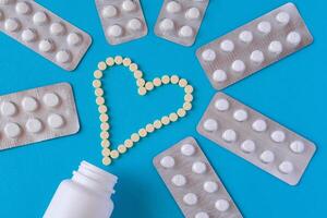 Yellow tablets are laid out in the shape of a heart, white jar surrounded by a pills in blisters on a blue background photo