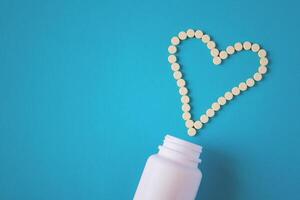 Yellow tablets are laid out in the shape of a heart and white jar on a blue background with copy space photo