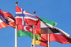 Close up view of a flags of different countries flutters in the wind against a clear blue sky photo