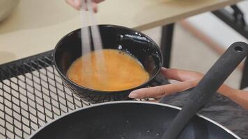 detailed shot of a woman's hand adding salt to the egg she is frying in a frying pan on the burner of a gas stove in a Colombian kitchen. video