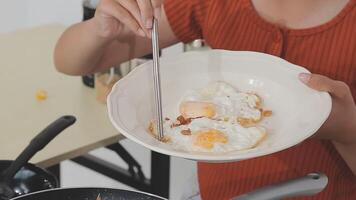 detailed shot of a woman's hand adding salt to the egg she is frying in a frying pan on the burner of a gas stove in a Colombian kitchen. video