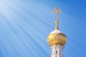 Gilded dome of a Christian temple illuminated by rays of sun against a bright blue sky with copy space photo
